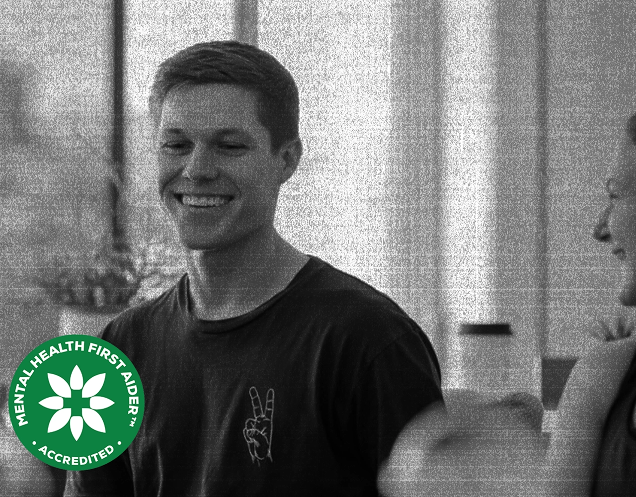 A workshop participant smiling during a session, with an accredited Mental Health First Aider badge
