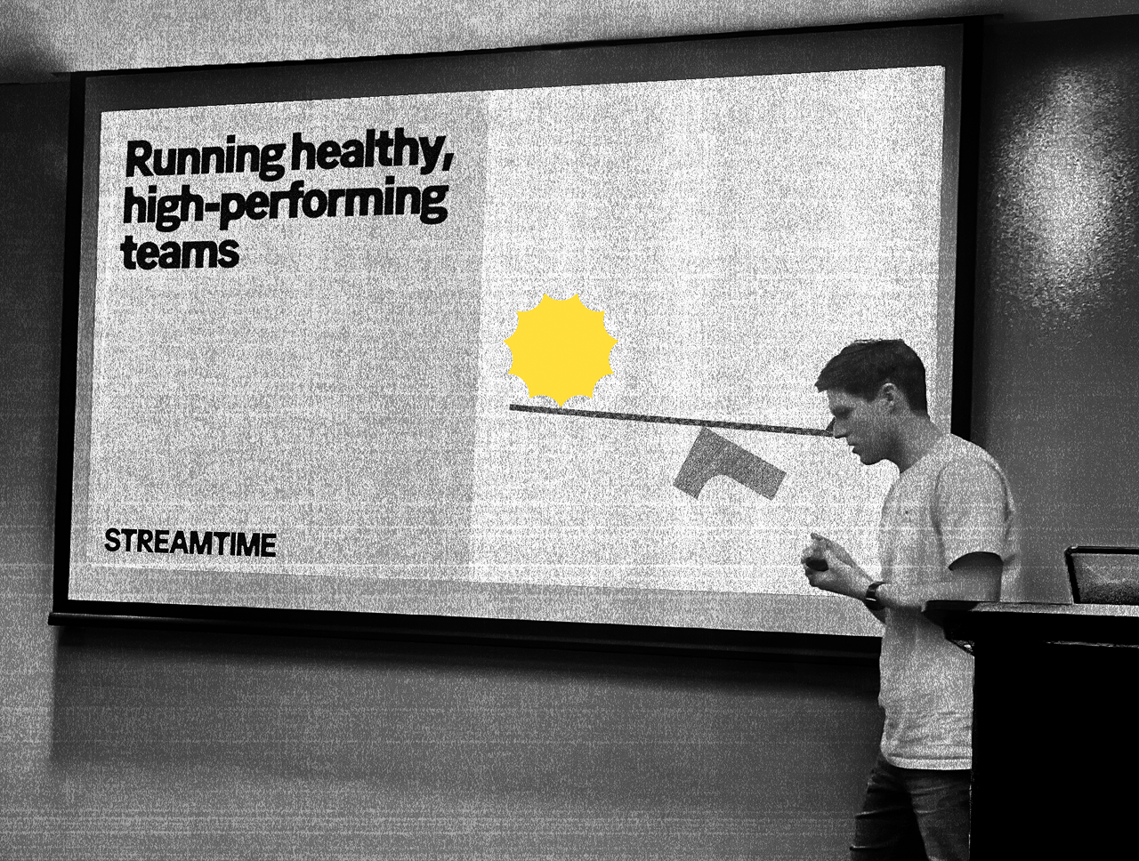 A presenter beside a screen reading Running healthy, high-performing teams