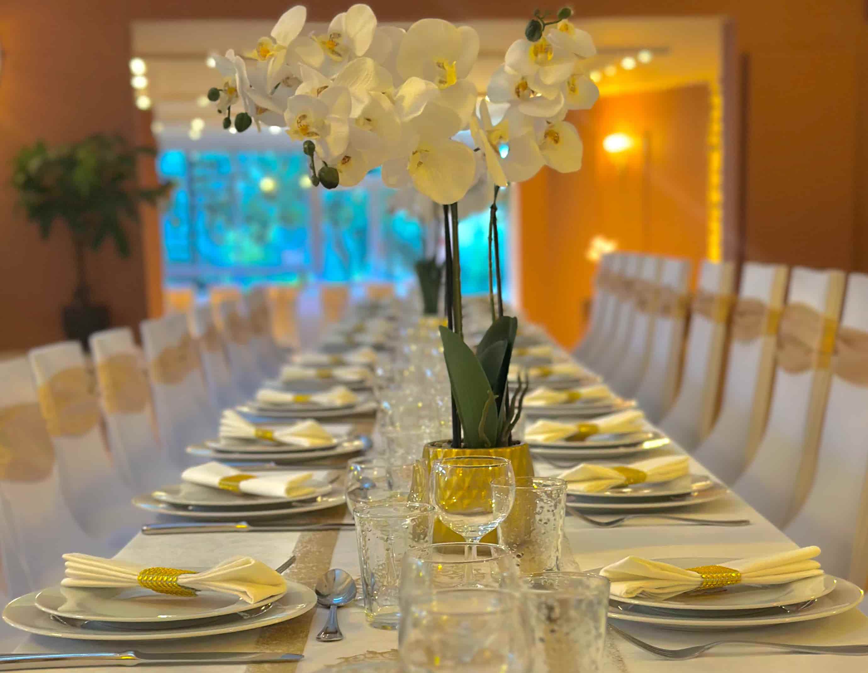 Table de réception avec de la vaisselle blanche et dorée ainsi qu'une orchidée blanche dans la salle de séminaire et célébrations