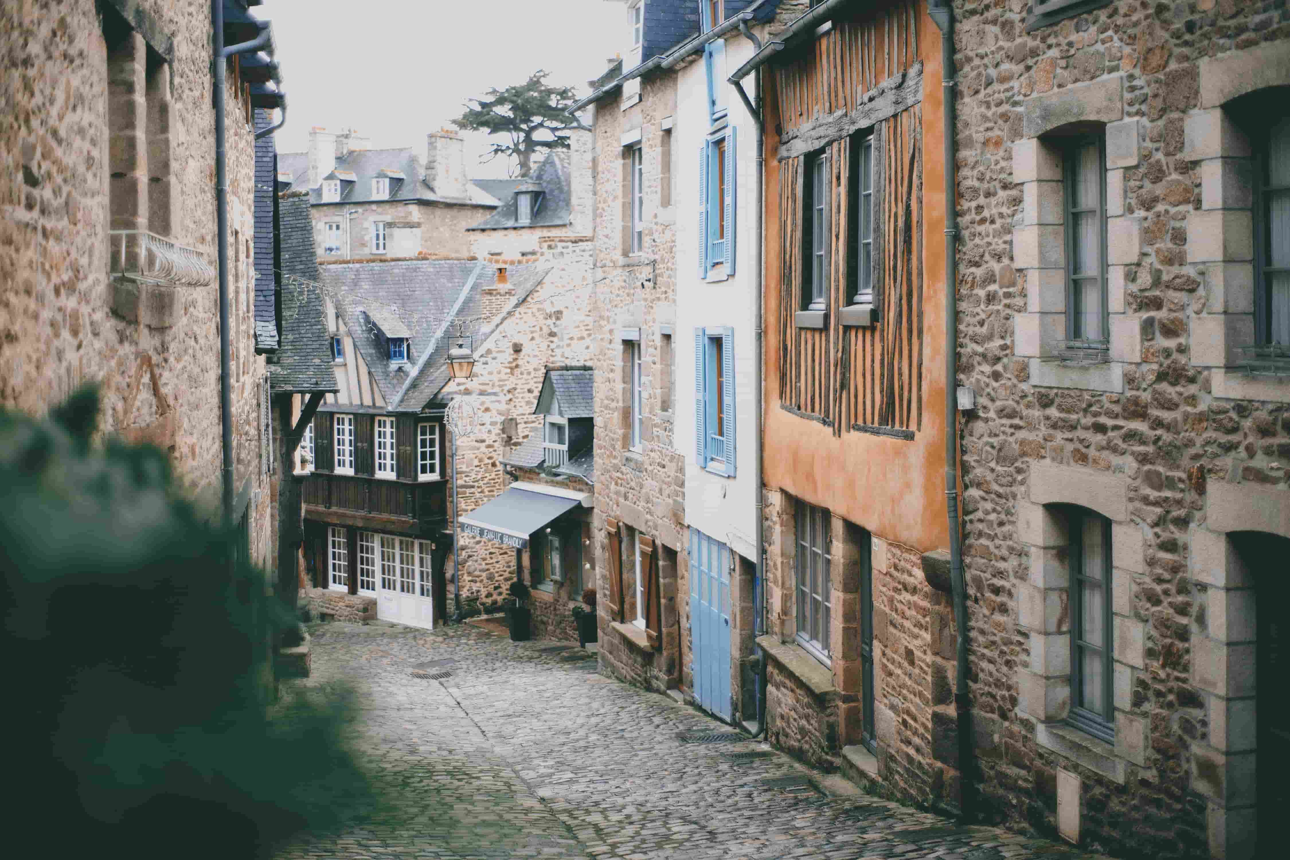 Vue pittoresque d'une ruelle pavée bordée de maisons en pierre aux façades colorées, typiques des villages médiévaux français. Les bâtiments sont dotés de fenêtres à volets bleus et d'éléments en bois apparents, créant une atmosphère charmante et intemporelle. Cette image illustre l'ambiance d'un village français traditionnel, semblable à Montfort-l'Amaury.