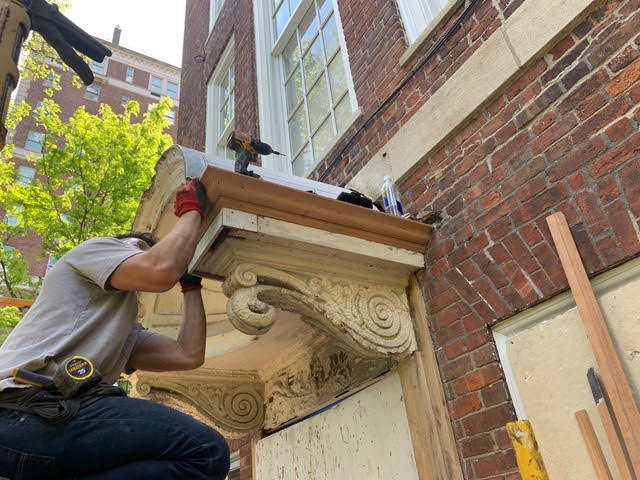Craftsman restoring decorative wood window cornice on historic brick building