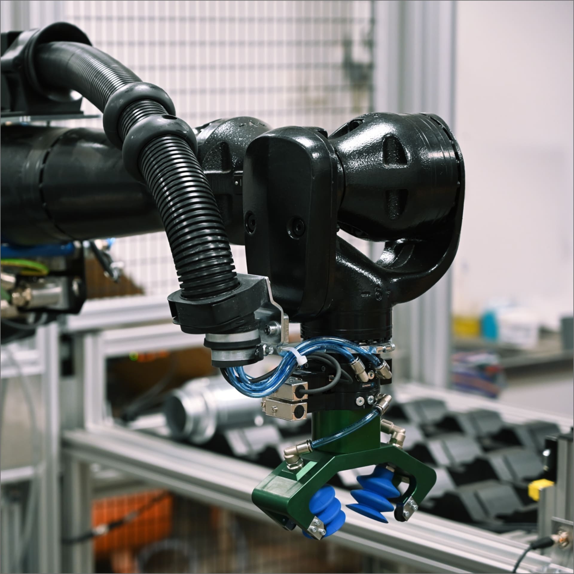 Industrieroboterarm mit schwarzen Komponenten und blauen Sauggreifern in moderner Fertigungsumgebung.
