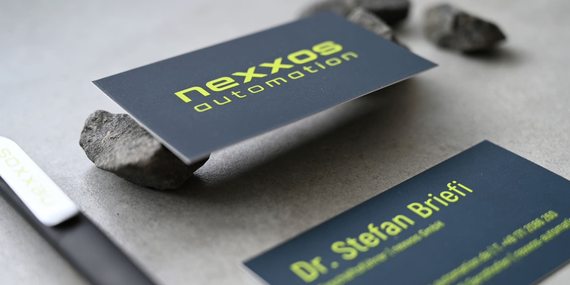 Nahaufnahme der Visitenkarte von nexxos automation mit gelbgrünem Logo auf dunkelblauem Grund.