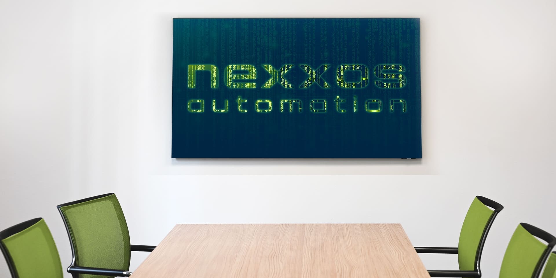 Leerer Besprechungsraum mit Holztisch und grünen Stühlen, an der Wand ein grosser Bildschirm mit gebrandetem nexxos automation Bildschirmhintergrund im Matrixstil.