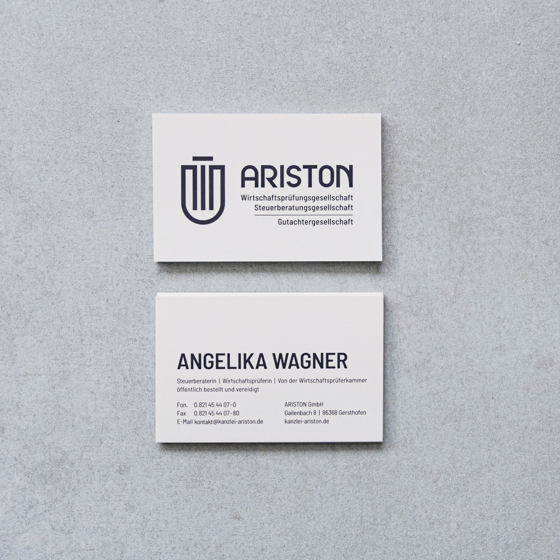 Zwei Visitenkarten auf grauer Fläche. Oben ARISTON-Logo mit Firmenbezeichnung, unten Kontaktdaten und Berufsbezeichnungen von Angelika Wagner.