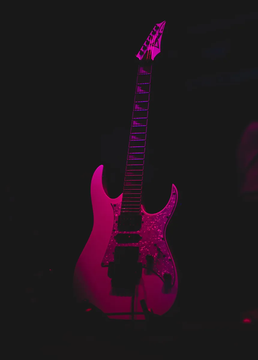 Electric guitar illuminated with pink lighting against a dark background.