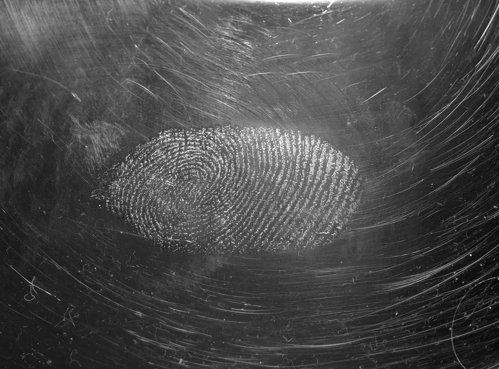 Close-up of a fingerprint on a scratched metallic surface in black and white.