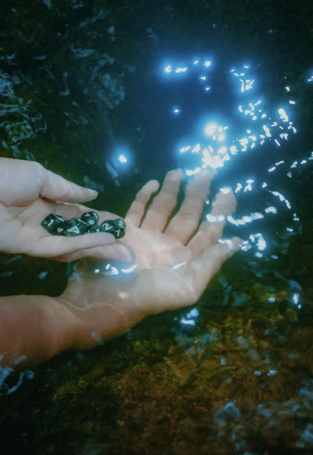 Two hands submerged partially in water, one holding black polyhedral dice with white numbers.