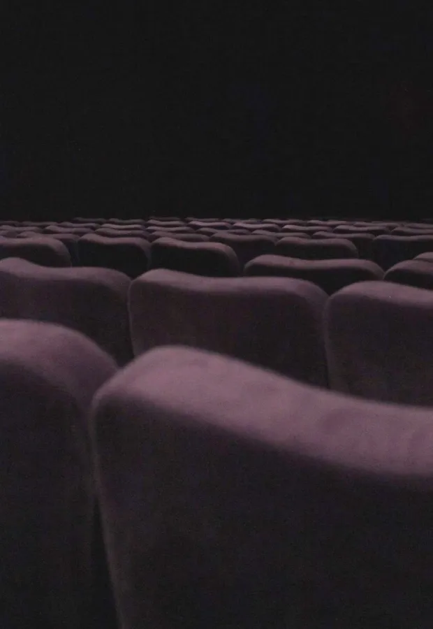 Rows of empty dark purple theater seats facing a dark, unlit stage or screen.