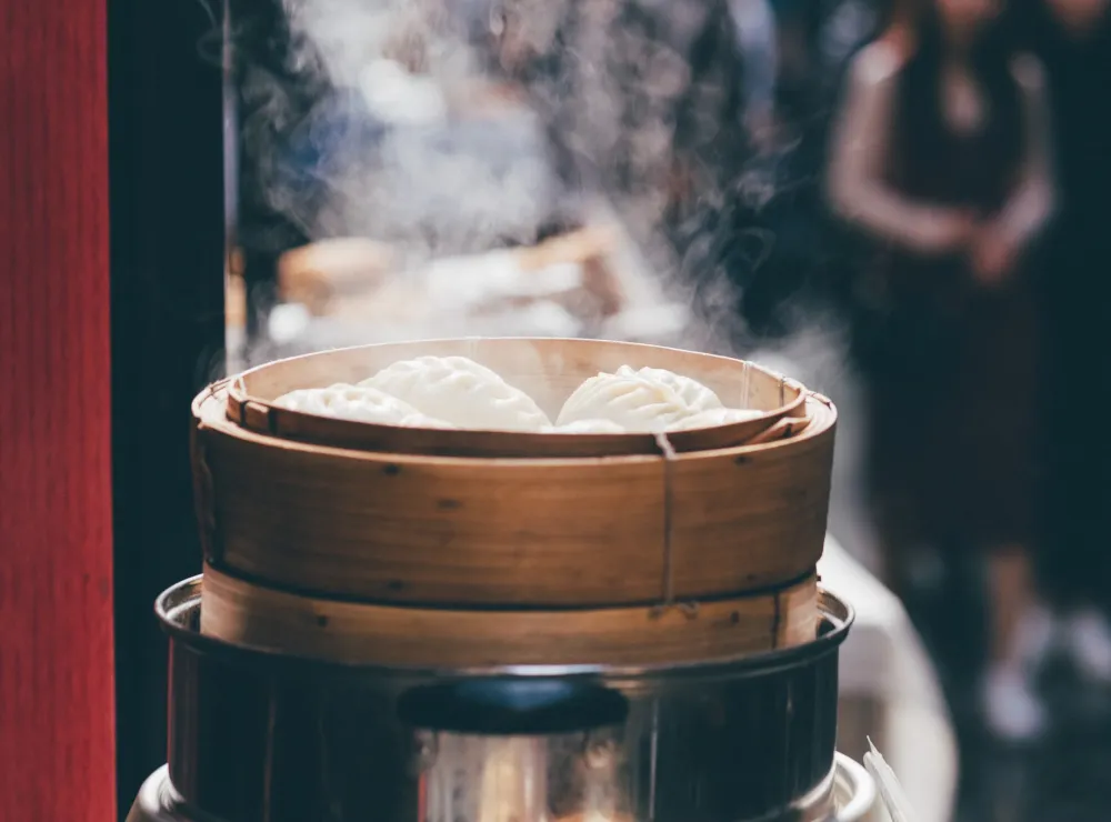Steaming bamboo basket with white dumplings inside.