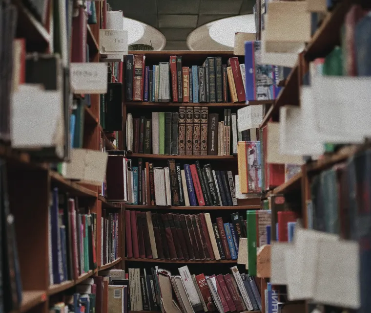 A library aisle with wooden shelves filled with books and catalog cards hanging on strings.