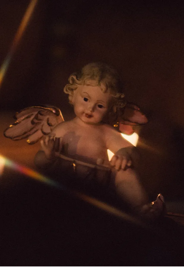 Close-up of a cherubic angel figurine with curly hair and wings, softly illuminated in dim light.