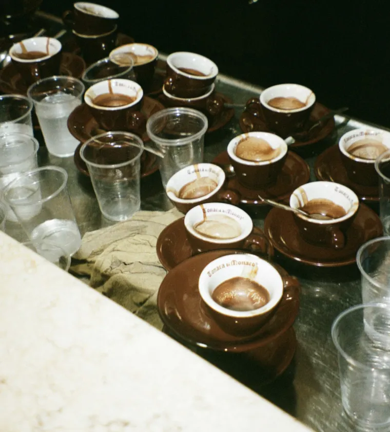 Multiple brown ceramic espresso cups with remnants of coffee arranged on a surface alongside several clear plastic cups containing water.