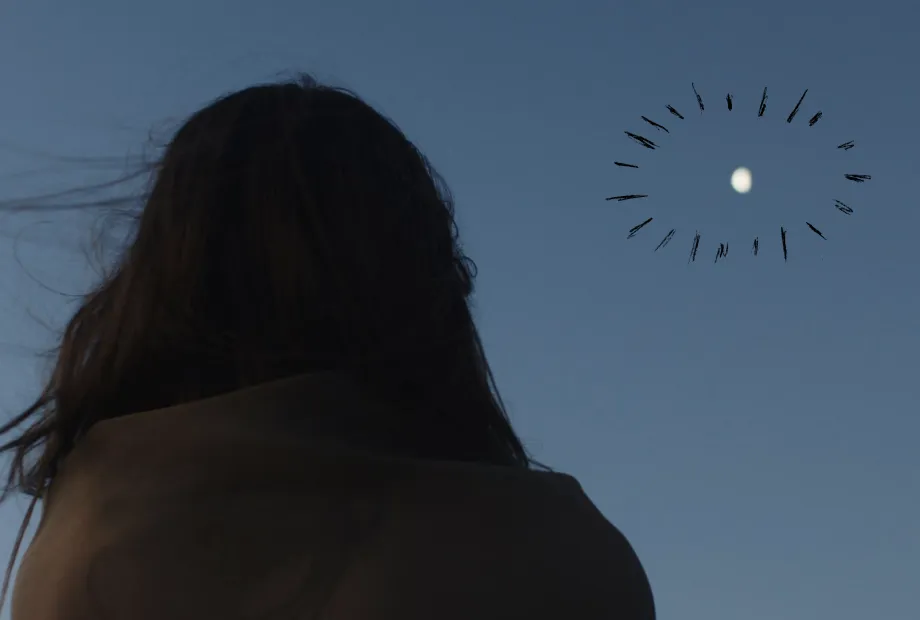 Silhouette of a person with long hair looking at the moon in a clear dusk sky.