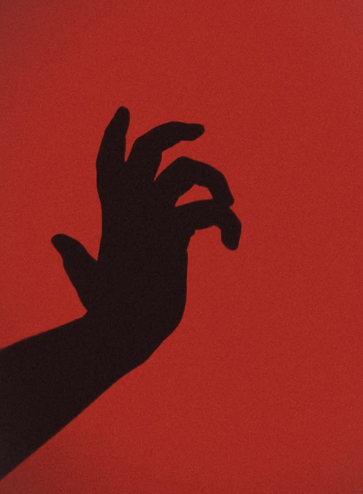 Shadow of a hand against a red background with fingers curled.