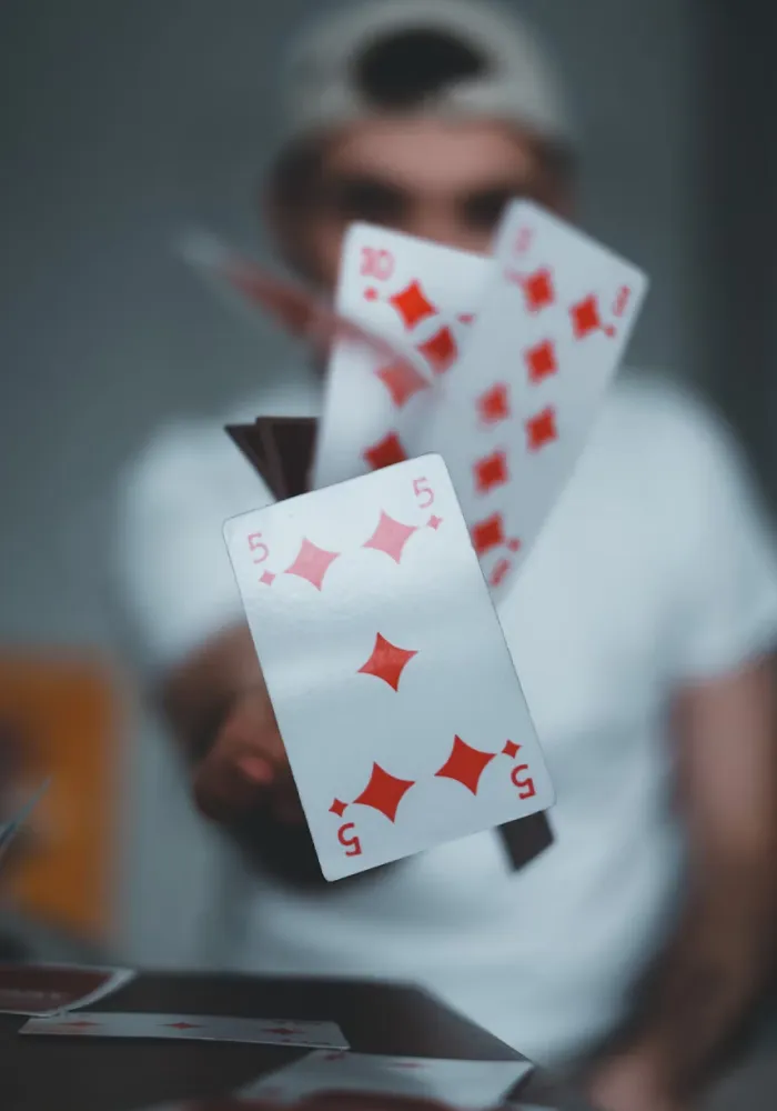 Playing cards including five, ten, and seven of diamonds flying mid-air in front of a person wearing a white shirt and cap.