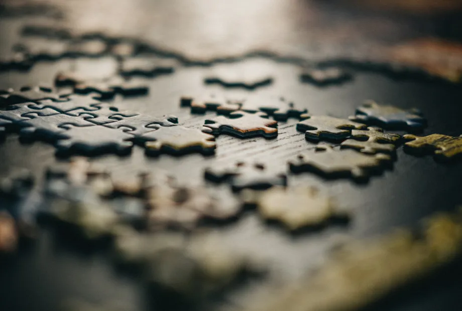 Close-up of scattered puzzle pieces on a dark surface with shallow depth of field.