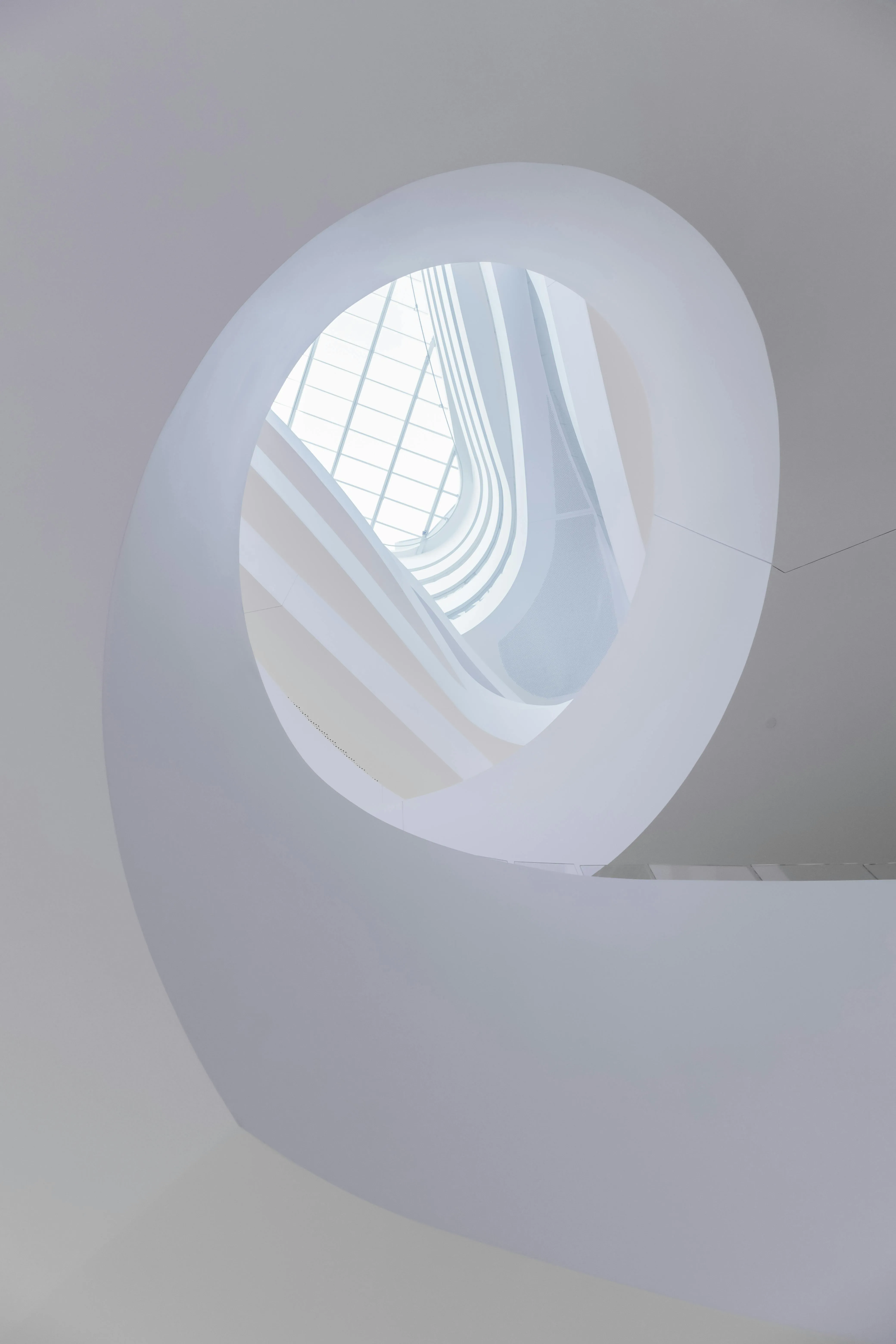 Abstract upward view of a modern white spiral staircase with a glass ceiling above.