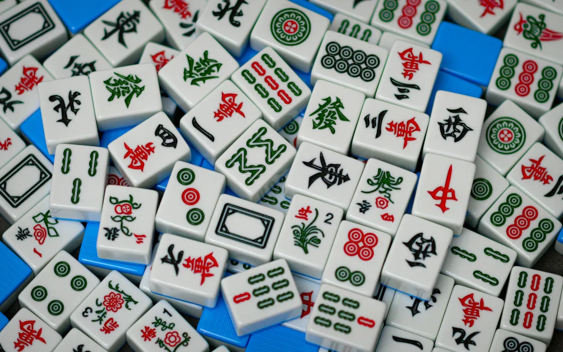 Close-up of scattered Mahjong tiles with various Chinese characters and symbols on a blue surface.
