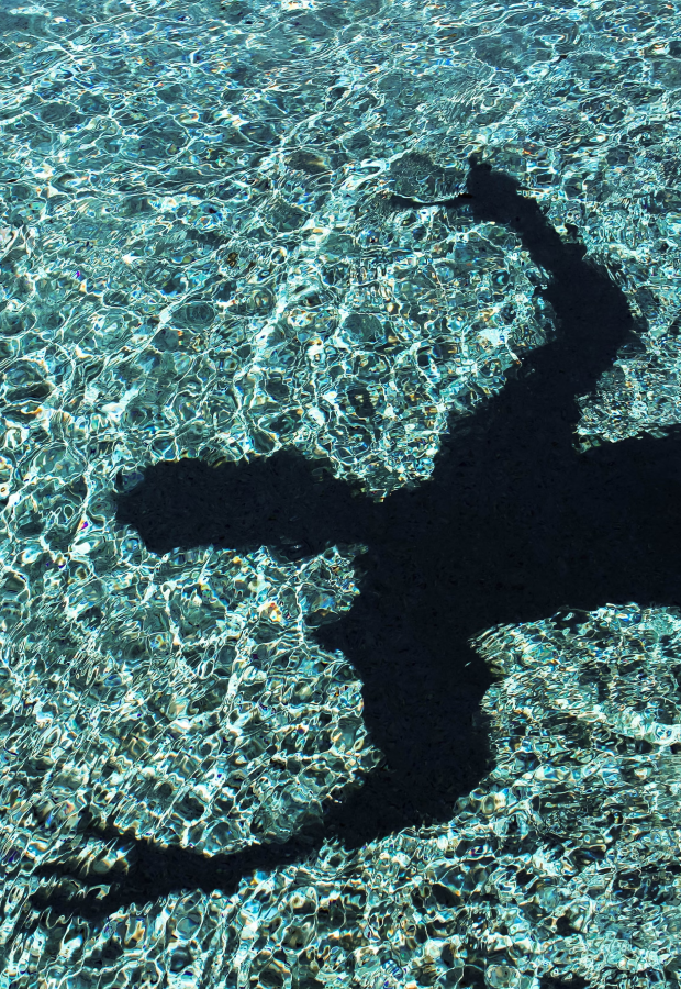 Dark shadow of a person with outstretched arms projected on rippling water surface.