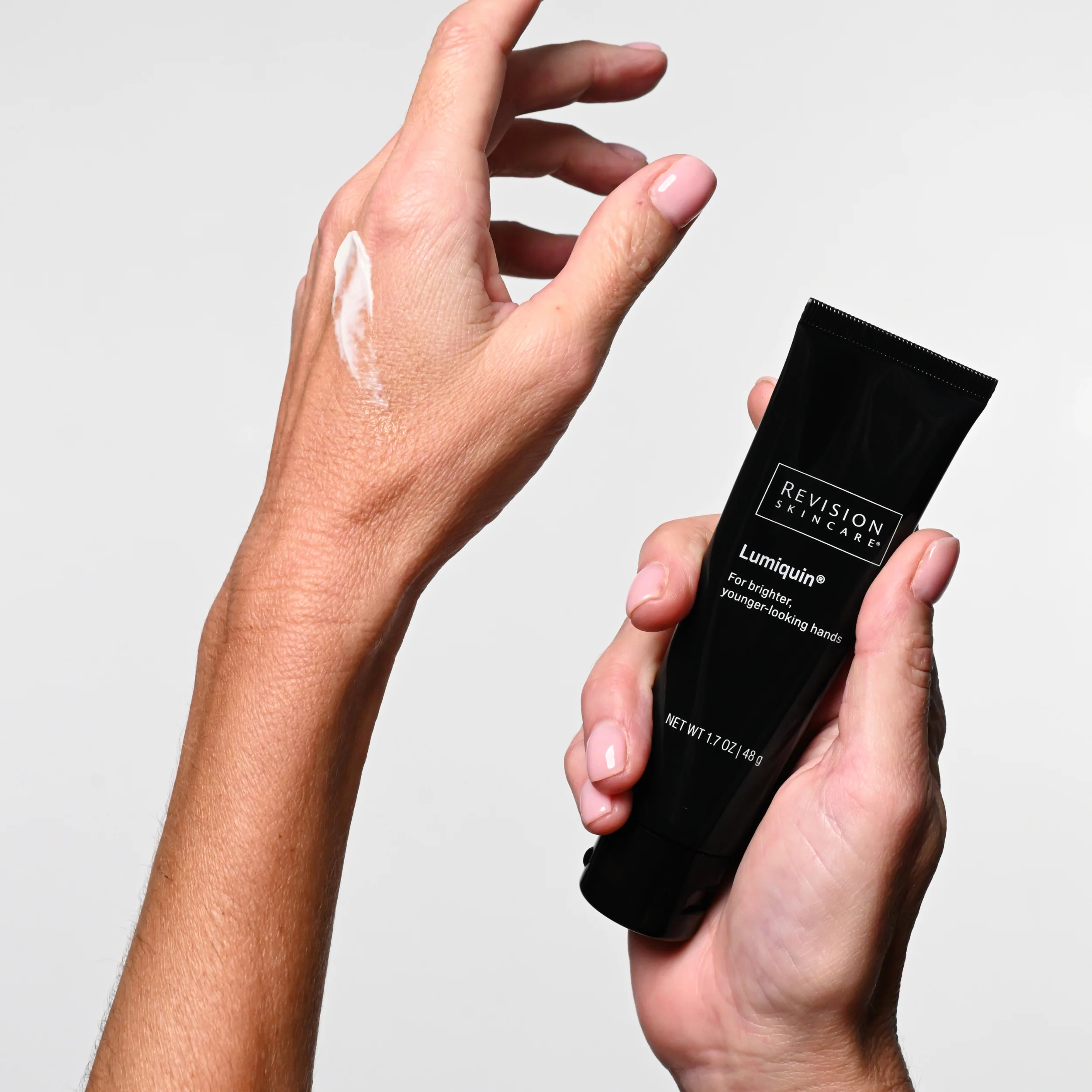 Two hands holding a tube of lotion and a tube of lotion.