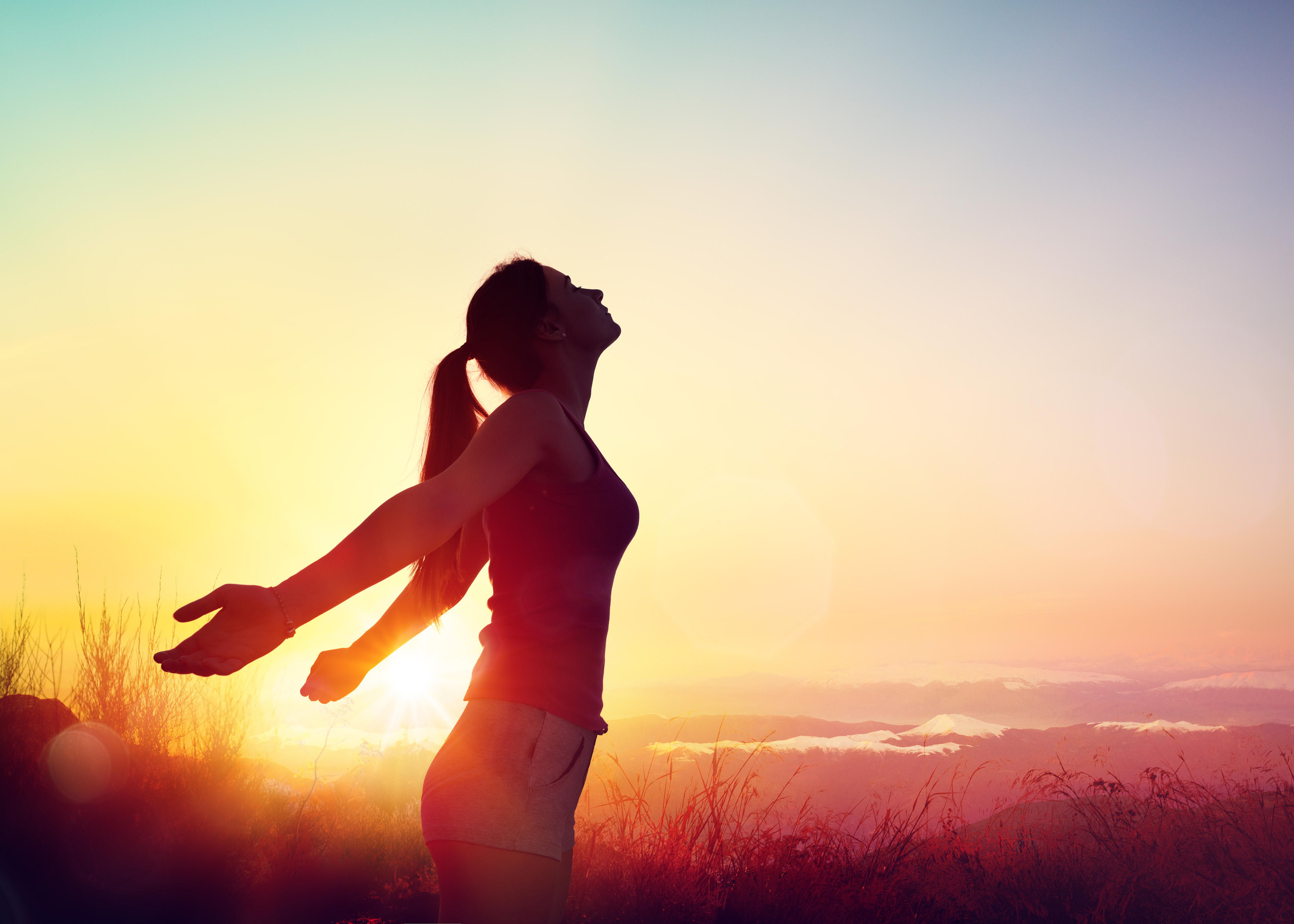 Silhouette of a woman with her arms back, basking in the sunrise.