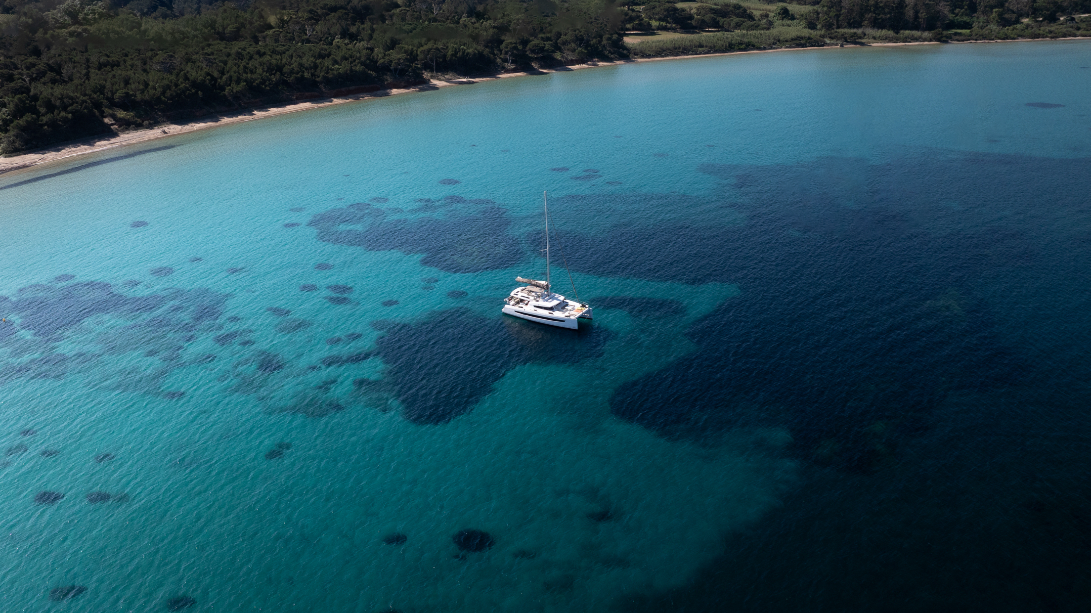Catamaran de luxe en navigation, photographié depuis les airs, sur l'eau turquoise.