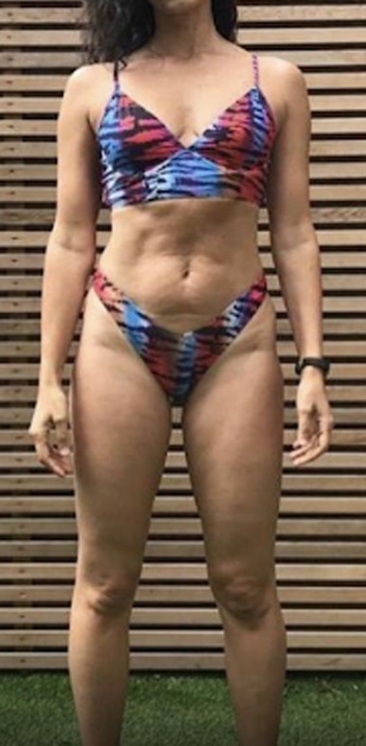 Woman standing outdoors wearing a blue, red, and black patterned bikini with a wooden slat background.