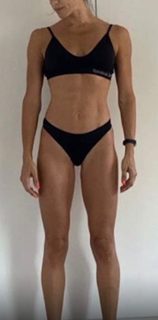 Woman standing against a plain wall wearing a black sports bra and matching black underwear.