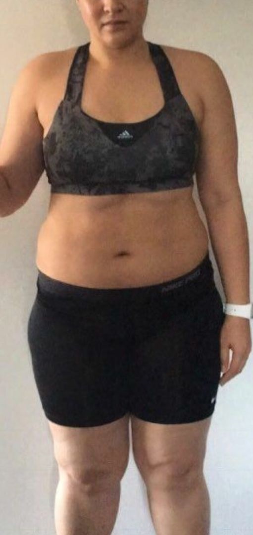 Front view of a person wearing a black sports bra and black shorts standing against a plain background.