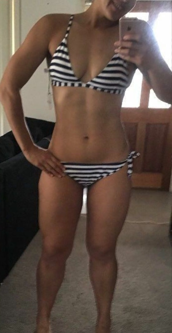 Person wearing a black and white striped bikini, taking a mirror selfie in a room with carpeted floor and wooden door.