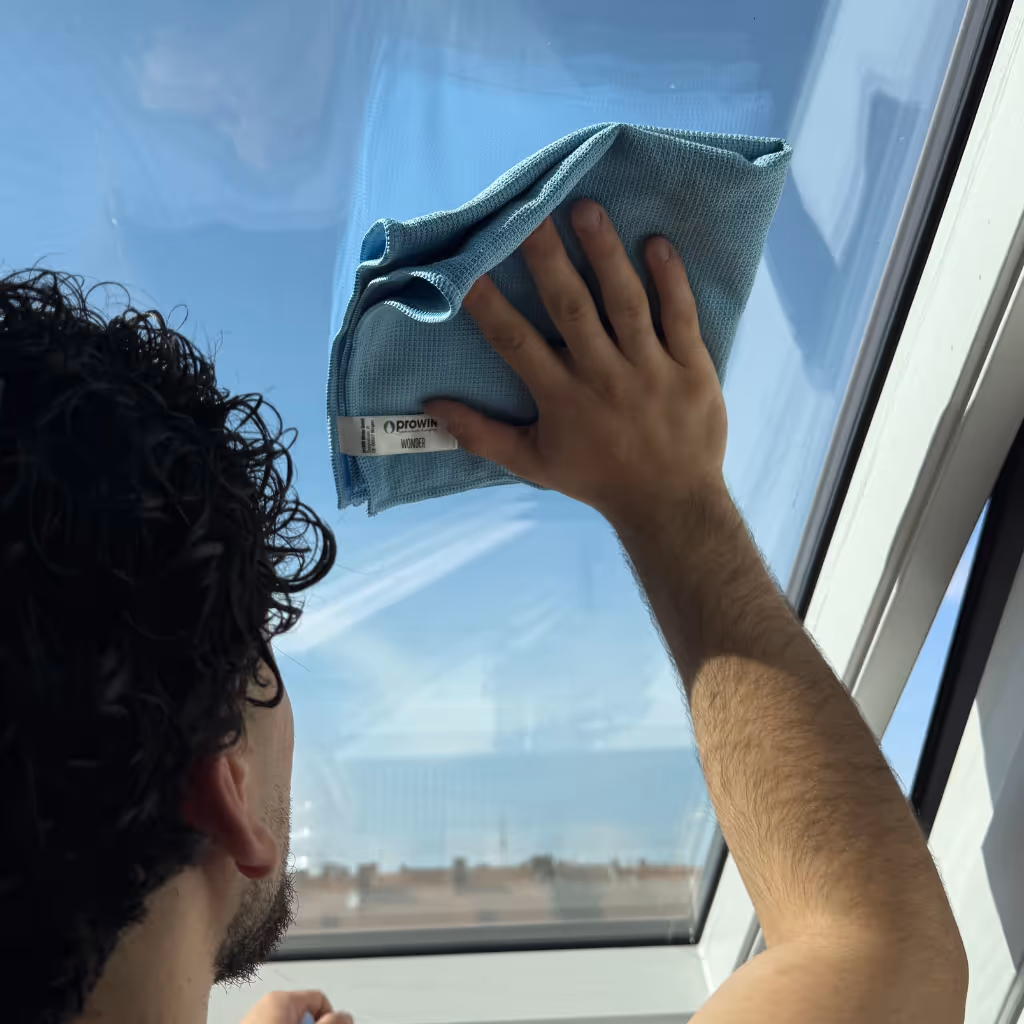 Mann reinigt ein Fenster mit einem Mikrofasertuch von innen.