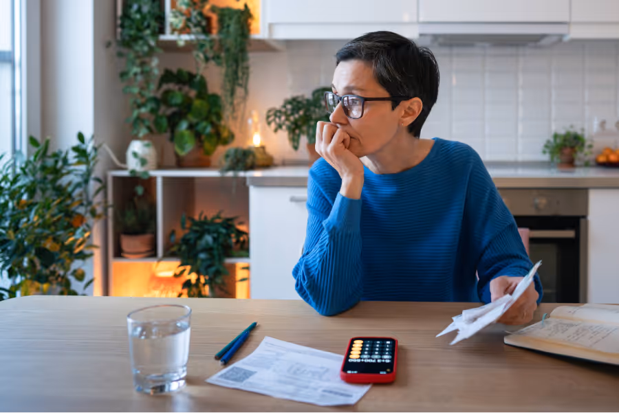 A middle-aged woman sitting on a chair is holding a coffee mug and smiling as she basks in sunlight
