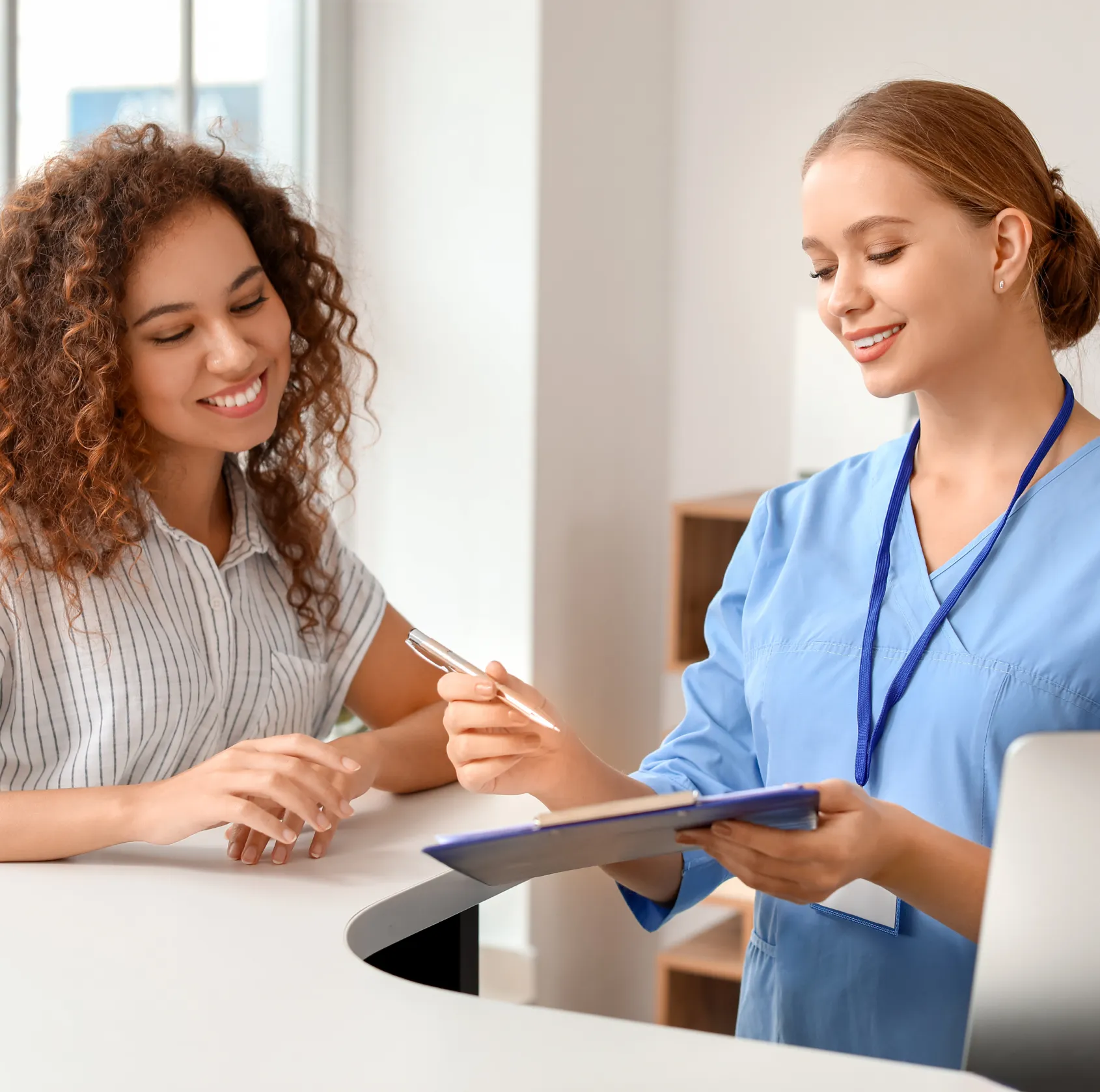 Two women in scrubs are sitting at a desk.