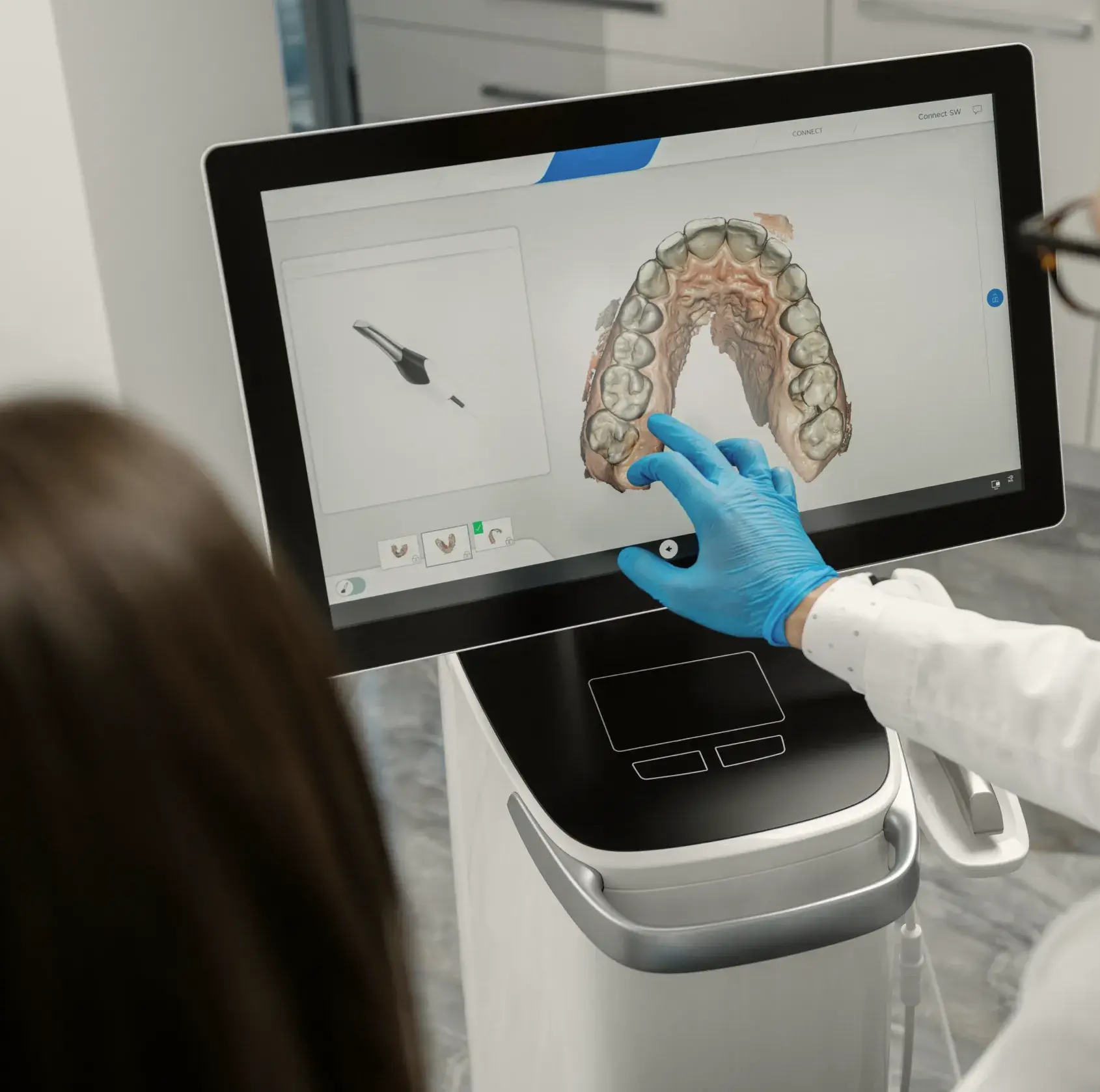 A woman in a white lab coat and blue gloves is looking at a computer screen.