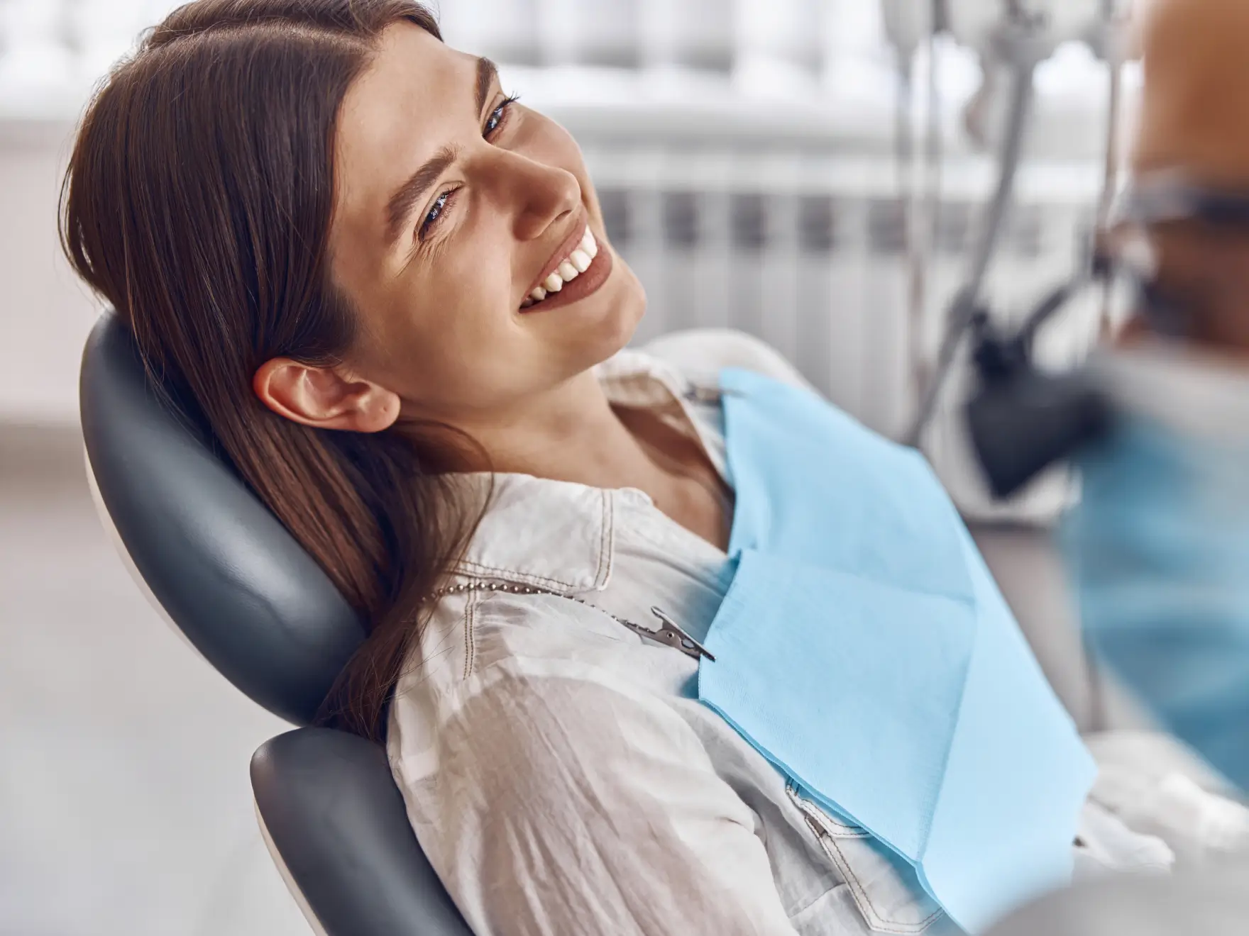 Woman smiling while sitting in a dentist's chair, wearing a dental bib.