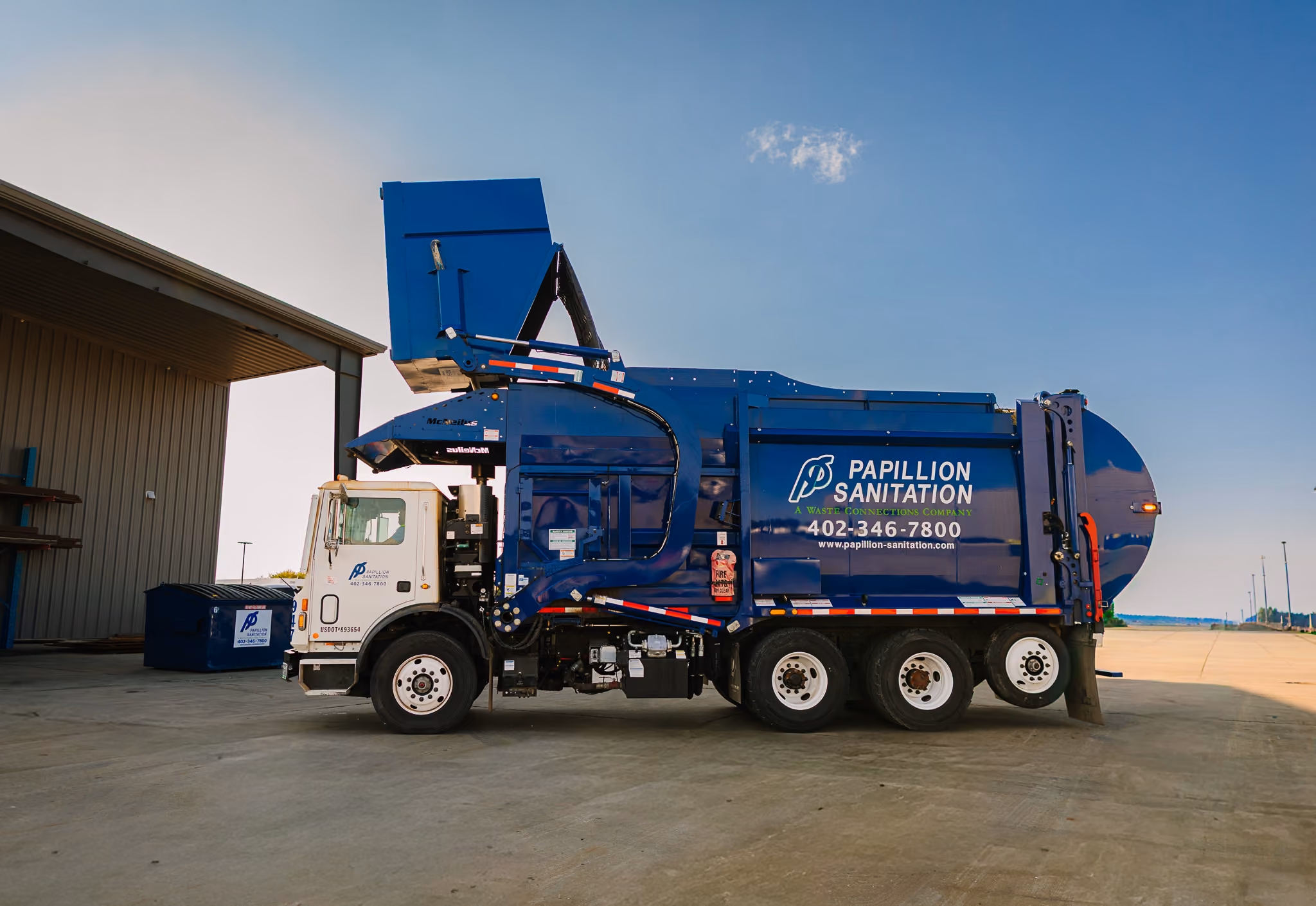 Front-load garbage truck servicing a commercial dumpster at a business location