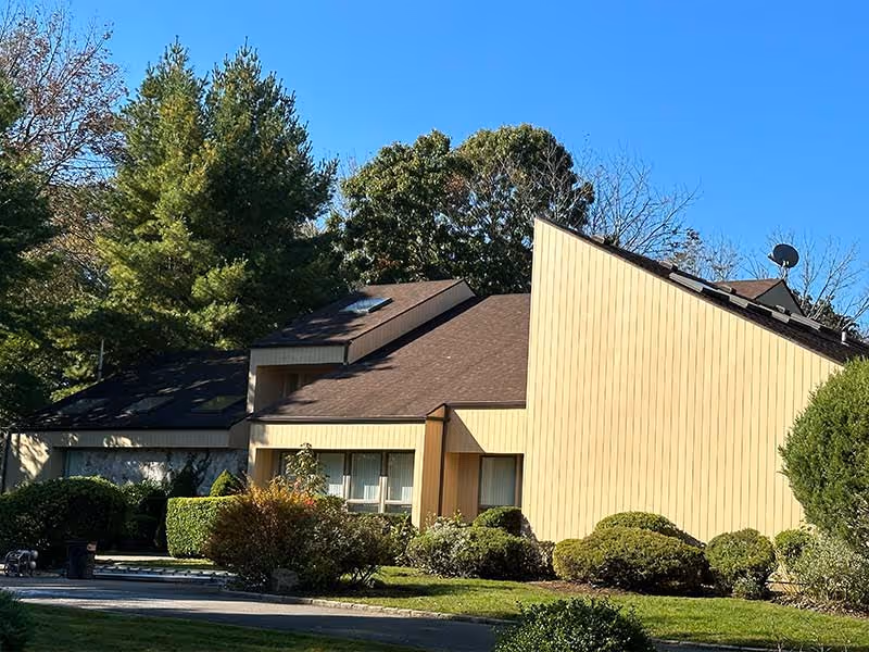Modern yellow house with angular design surrounded by green trees and landscaping