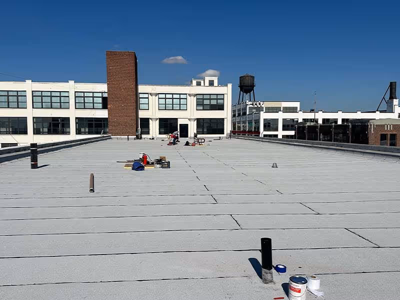 Workers on a flat roof with paint cans and equipment under blue sky