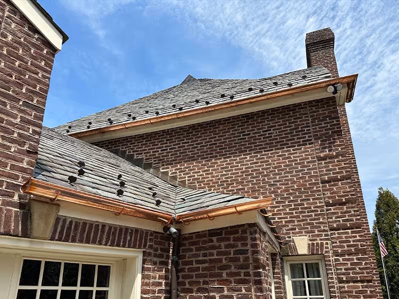 Brick house with slate roof and copper gutters against blue sky