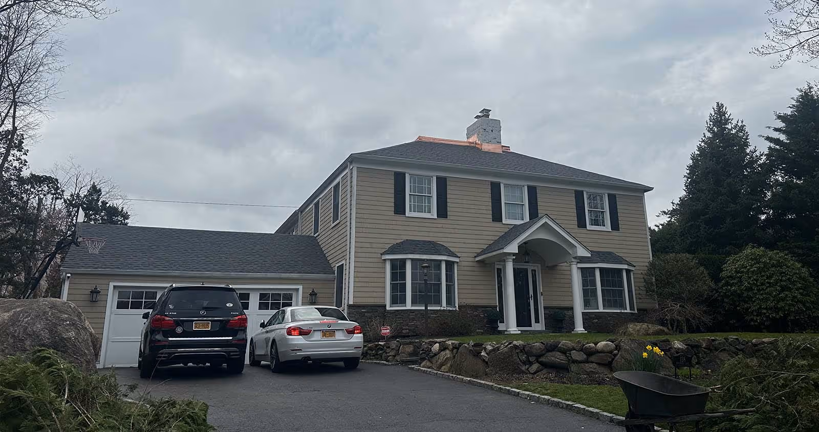 Two cars parked in front of a two-story suburban house on a cloudy day