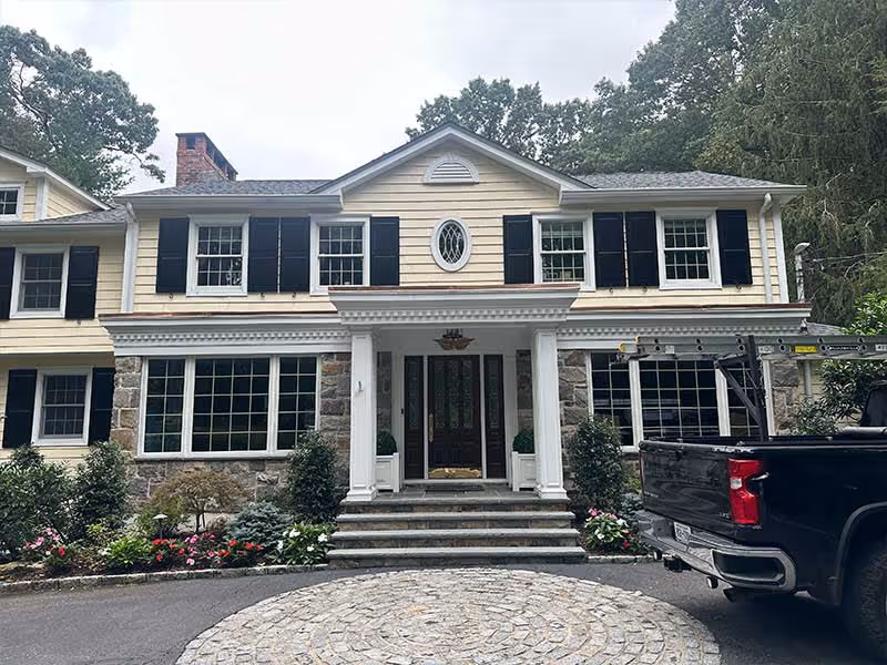 Traditional two-story house with stone base, black shutters, and flower gardens