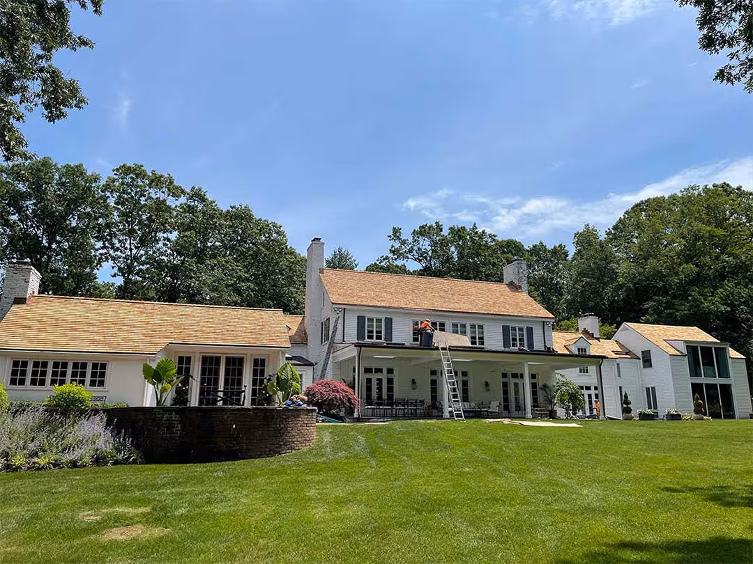 Large white house with new cedar wood shingle roof under sunny blue sky.