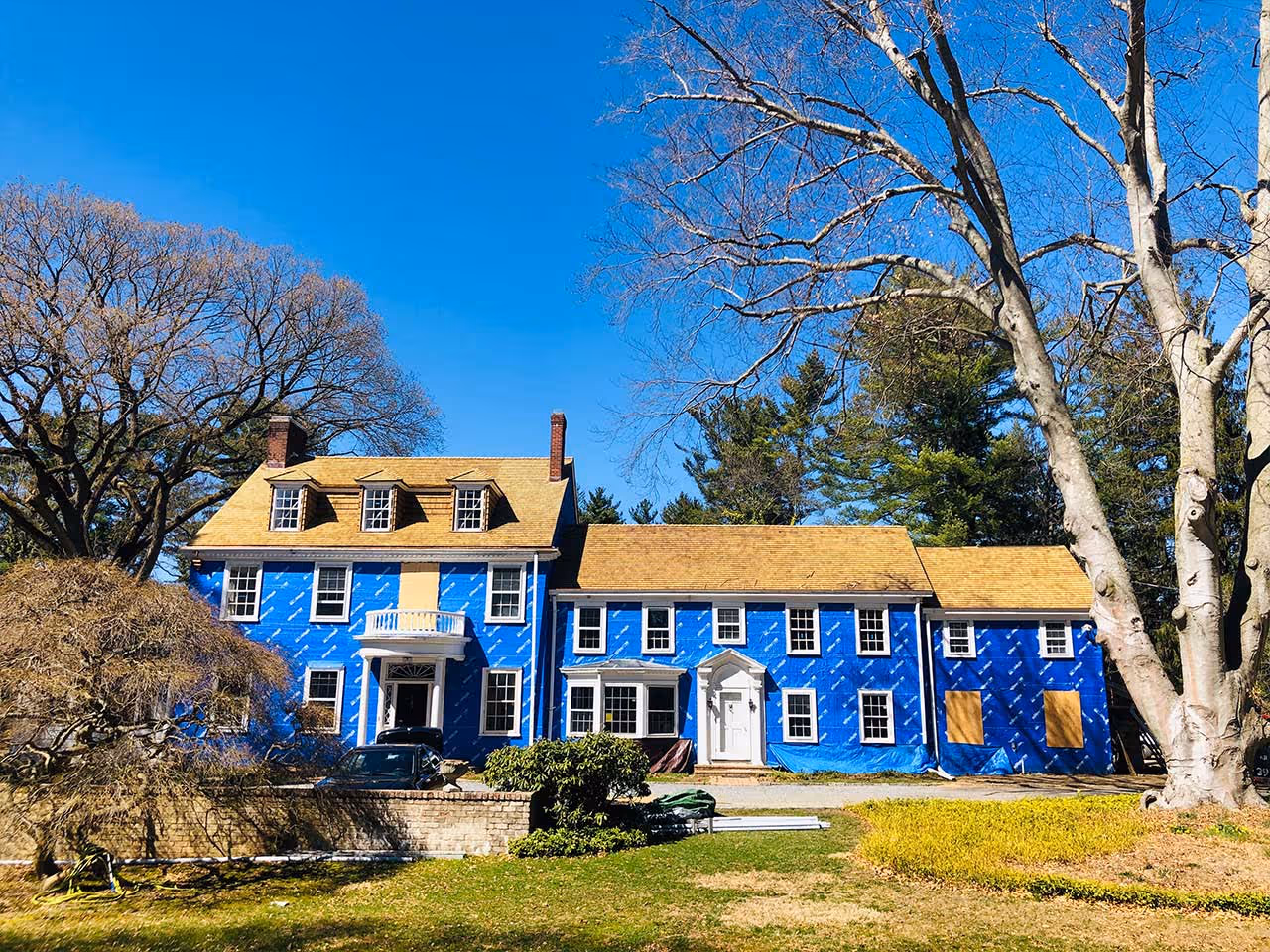 Large blue house under renovation with new cedar roofing and surrounded by trees on a clear day.