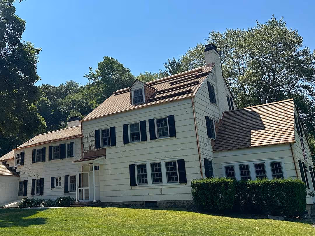 Large white two-story house with black shutters and new cedar roof shingles on a sunny day.