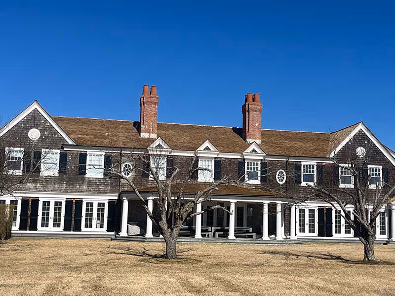 Large two-story house with cedar roofing, multiple chimneys, white columns, and a spacious front yard.