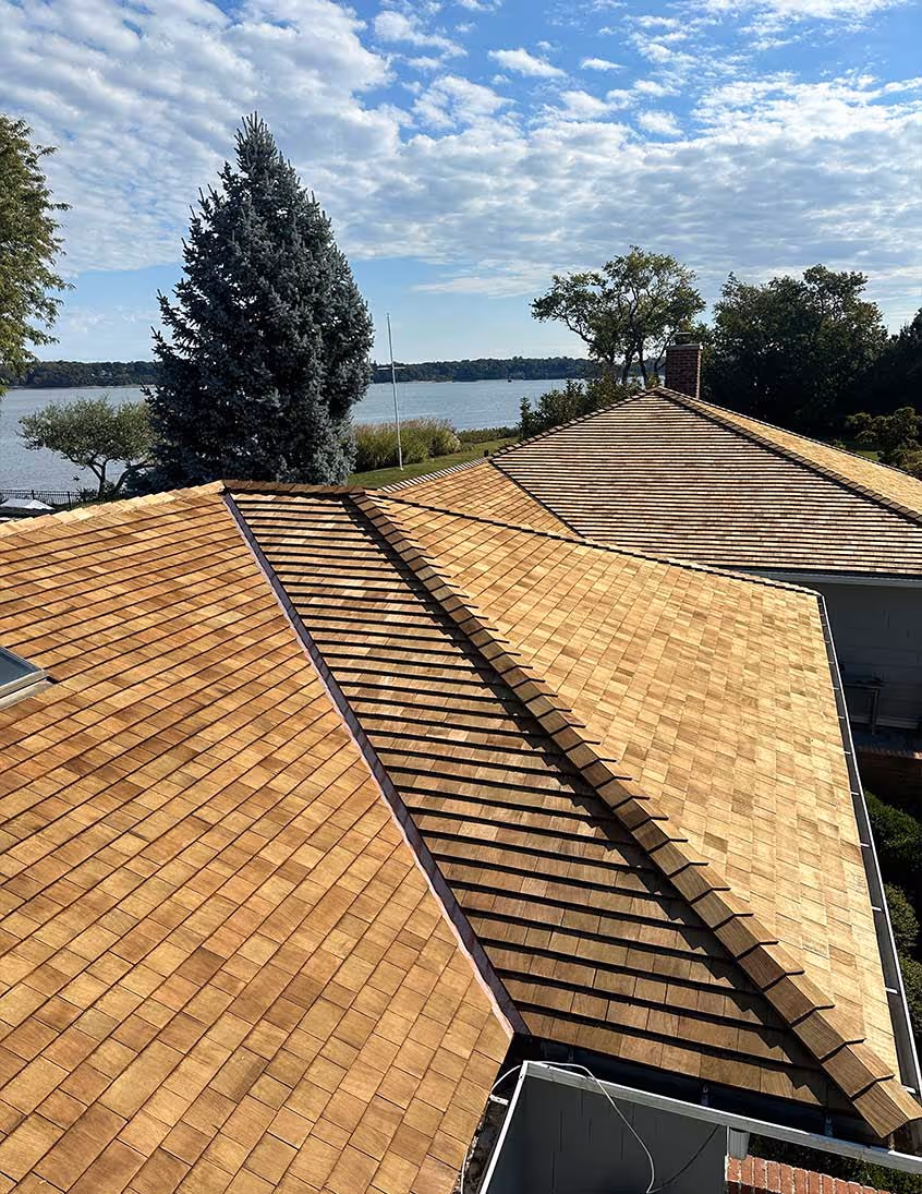 View of two houses with freshly installed cedar wood shingle roofs under a partly cloudy sky near a lakeside.