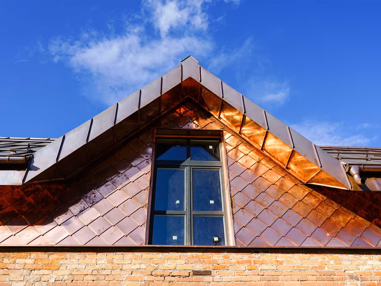 Copper metal roofing on a rooftop with a central rectangular window under a blue sky.