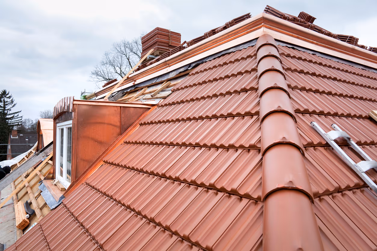 Copper metal roofing installation on a house under cloudy sky.