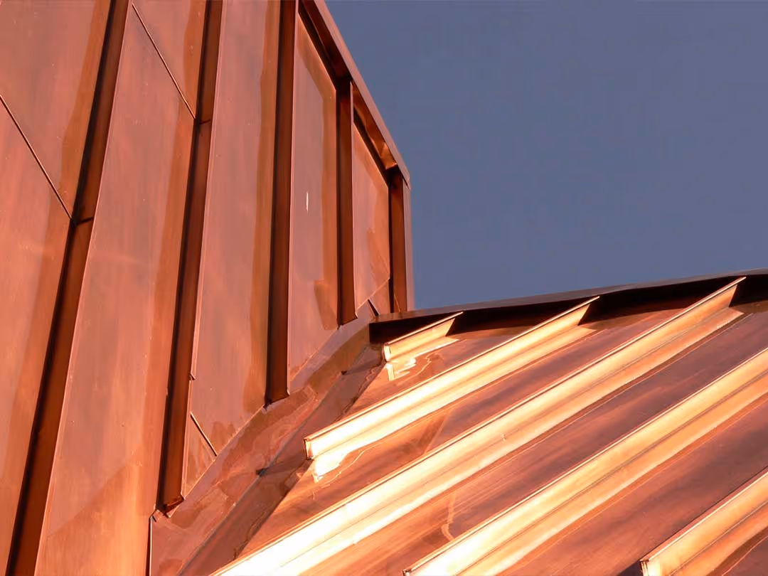 Close-up of a building corner with copper metal siding and roofing reflecting sunlight.